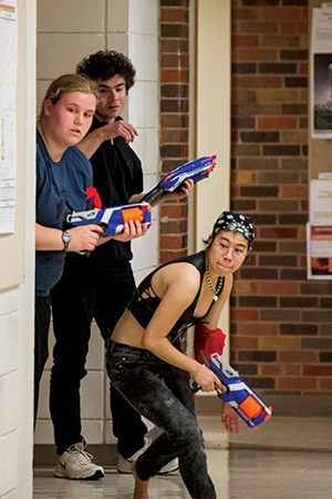 three players peer around a corner, nerf guns ready to take out their opponents