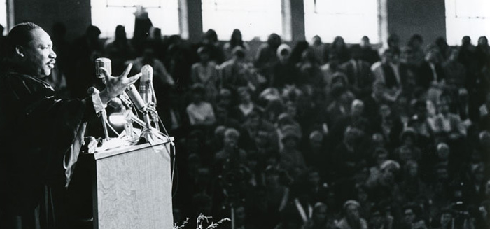 Martin Luther King Jr. preacing from a podium in Darby Gymnasium in front of a packed crowd