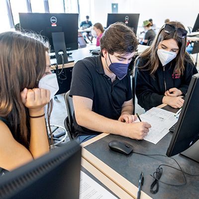 Three students in N95 masks at a bank of computers
