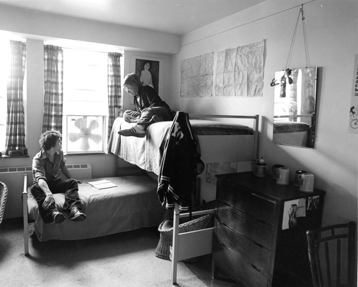 students sit on their beds, one bed lofted at an angle to the other