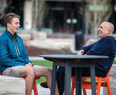 Lukas Roscoe and Robert Gehorsam laughing together at outdoor table