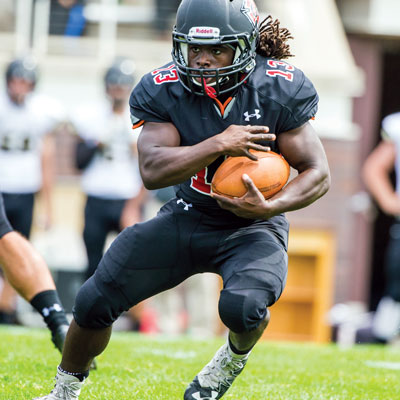 Grinnell football player protecting the ball while running