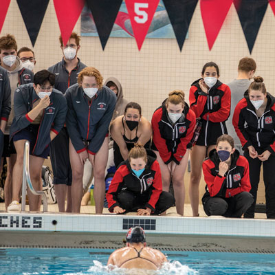 Grinnell swimmers watch their teammate from the side of the pool