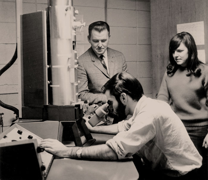 Walker with students in a biology lab with one student using the electron microscope