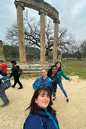 Four students pose for a selfie in front of a stone dais with carved columns