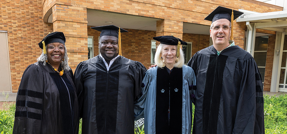 Four people in academic robes smiling at the camera