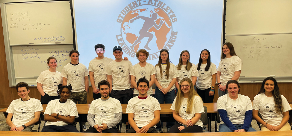 Students in matching tshirts pose in front of a SALSC logo in dark blue and bright red