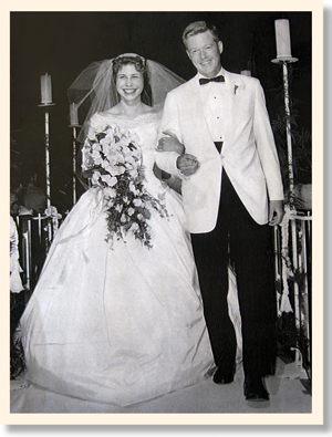 George in white jacket and black pants and Susan in wedding dress and holding bouquet
