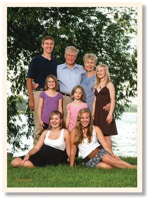 Family of eight pose in front of a tree and lake