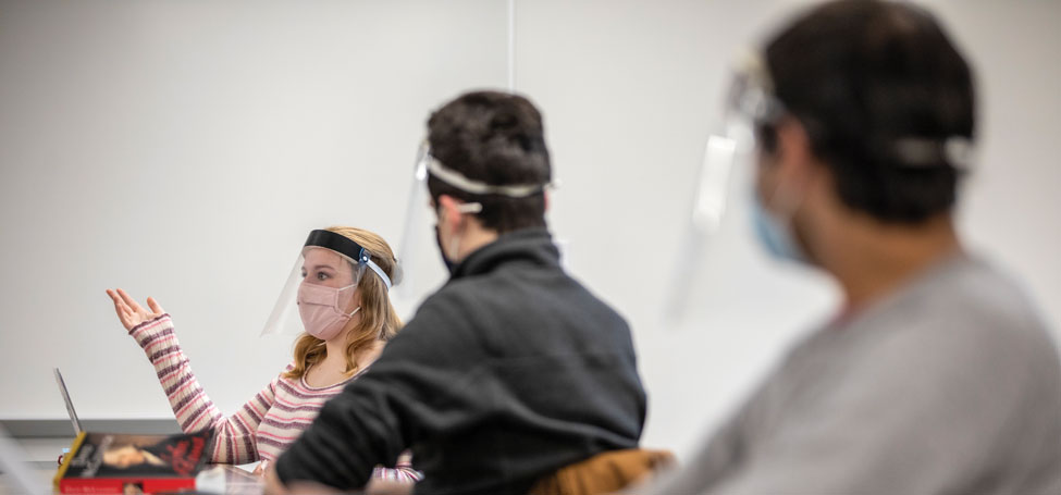 students in cloth masks and face shields talk in class