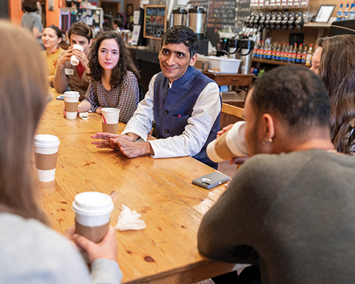 Several people with disposable coffee cups are gathered around a wooden table