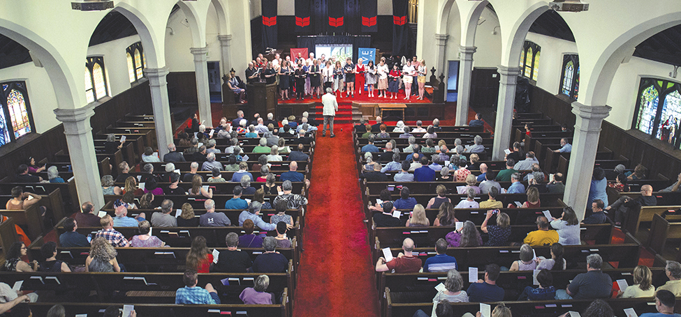 A choir stand at the altar of Herrick Chapel in front of a nearly full audience 