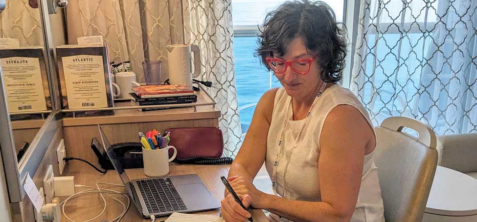Amy Goldmacher seated at a desk near an open door the sea visible outside