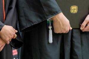 Close up of graduates hands as they stand side-by-side, one holding a diploma