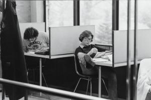black and white photo of students in small chairs at desks with short barriers to the front